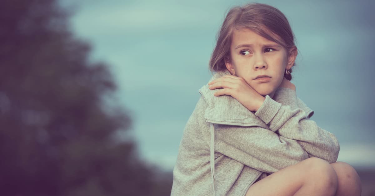 A young girl sitting, looking afraid, ashamed, and worried.